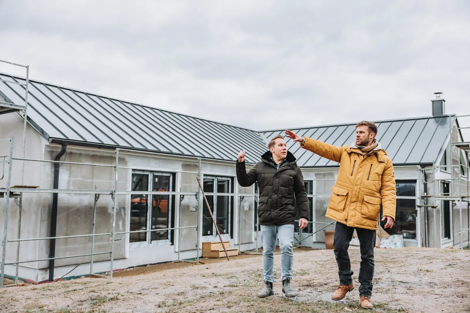 Marian und Felix gehen an einem Vendix-Haus im Rohbau vorbei und zeigen auf das Dach.
